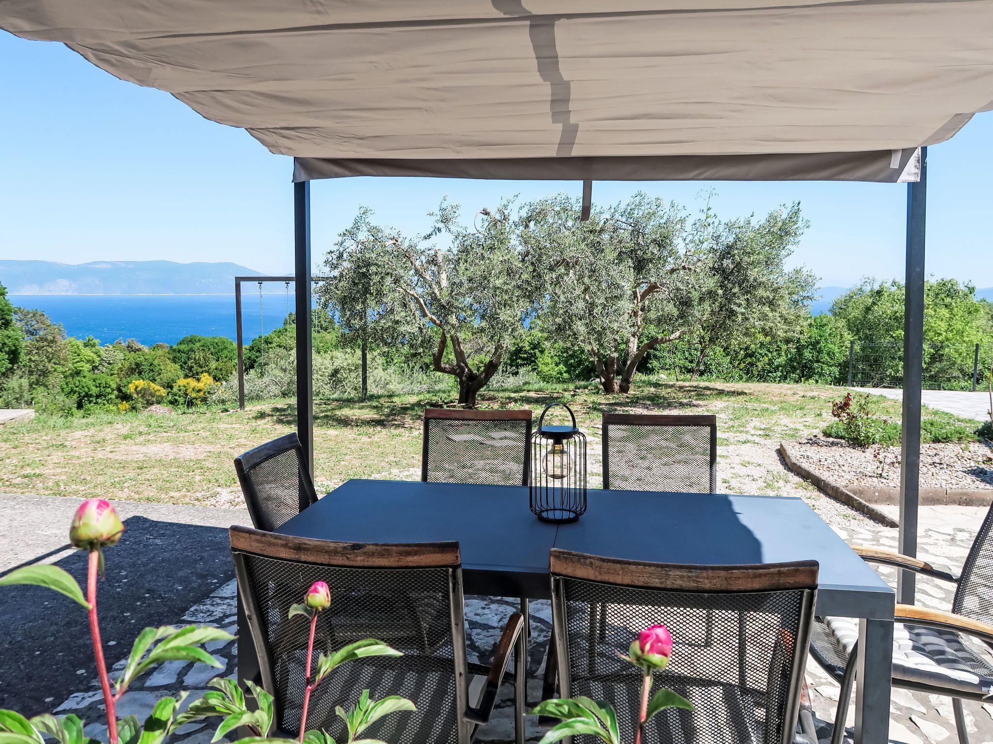 Un espace de restauration en plein air avec une table et des chaises, un auvent et une vue sur la mer et les arbres.