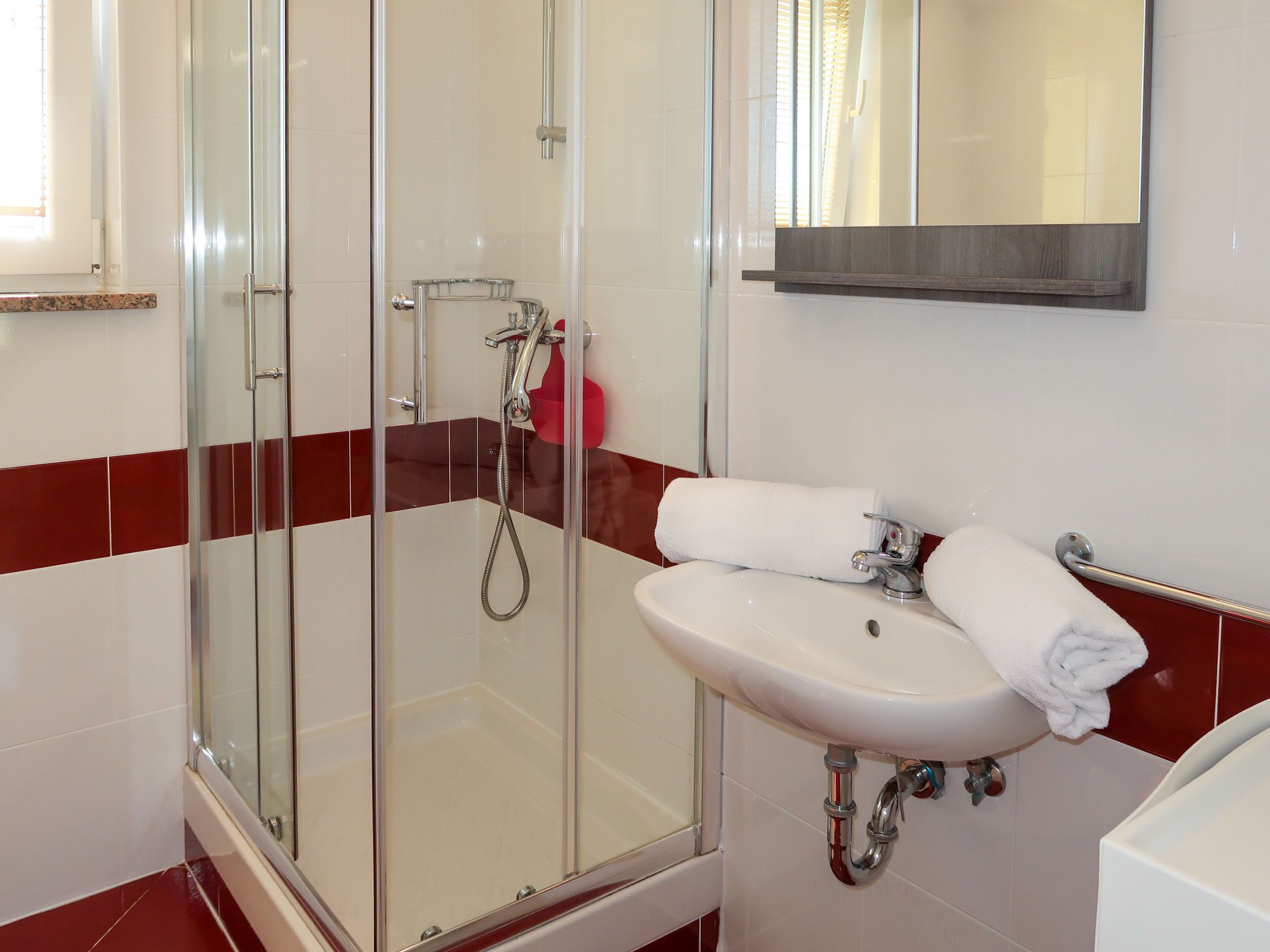A bathroom with a glass-enclosed shower, a white sink with a towel, and red-tiled walls.