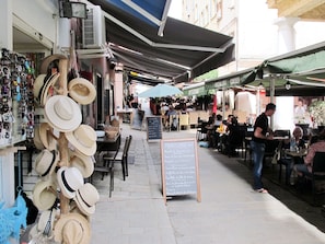 Un café al aire libre con mesas y sillas bajo sombrillas, un perchero para sombreros y un menú en una pizarra.