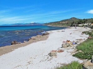 Una playa con aguas azules cristalinas, costa rocosa y gente tomando el sol.