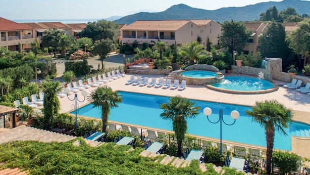 Un resort con piscina centrale, zone relax e uno sfondo montuoso.