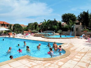 A swimming pool area with multiple pools, lounge chairs, and a stone water feature.