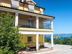 A two-story building with balconies, a patio area with a table and chairs, and a view of the sea.