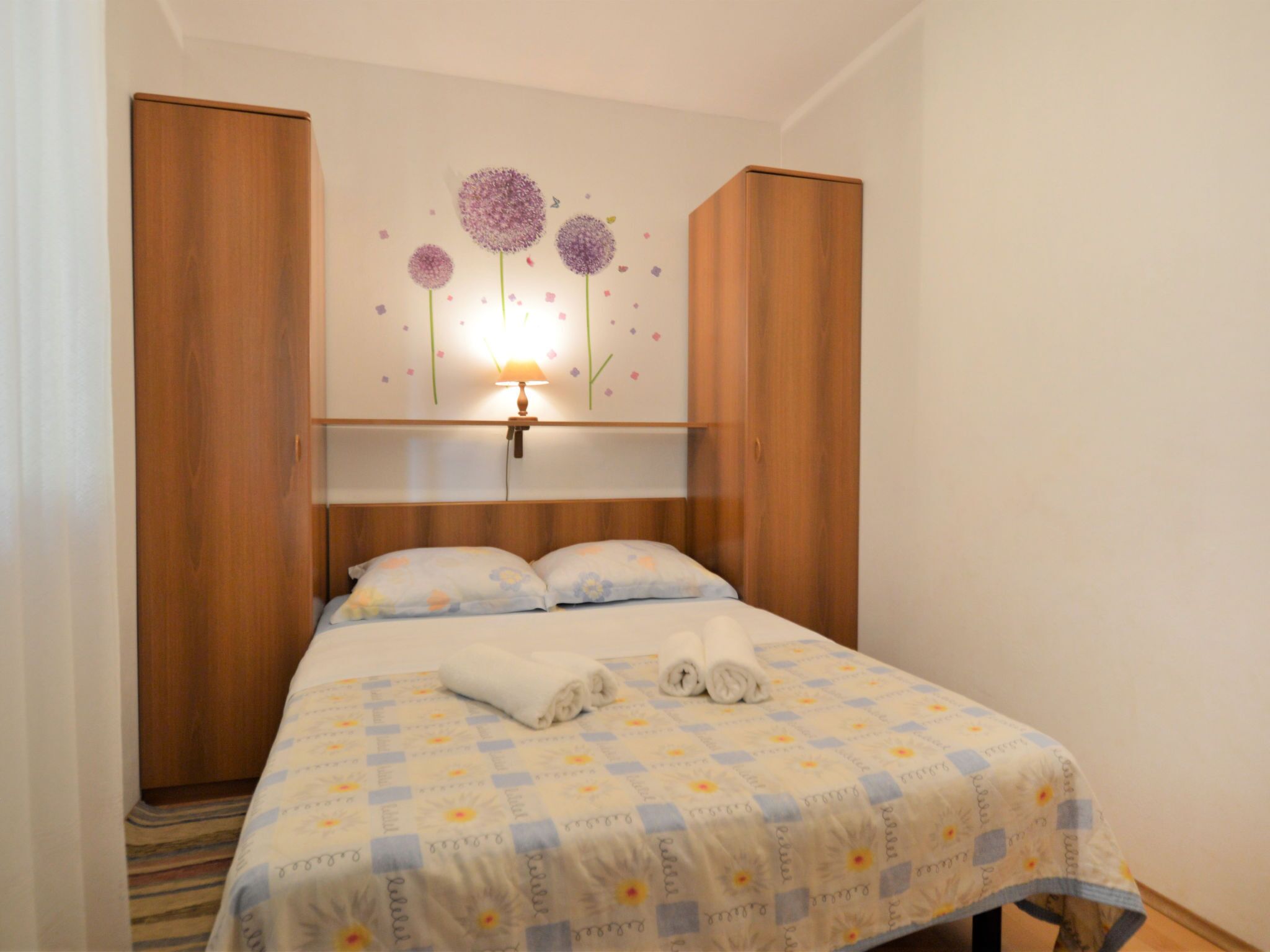 Un dormitorio con cama, armario de madera y una decoración floral en la pared.