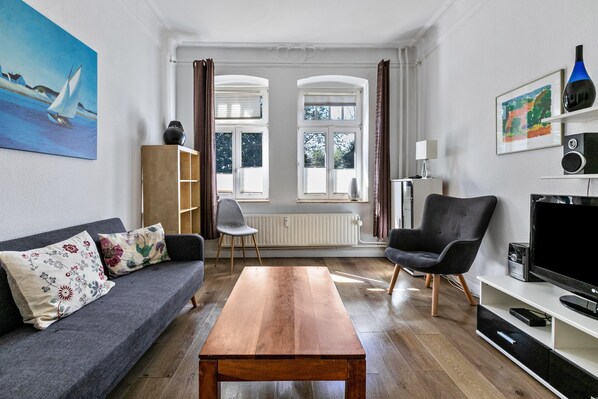 Ein Wohnzimmer mit einer Couch, einem Holztisch, einem schwarzen Sessel, einem Fernseher und einem Bücherregal.