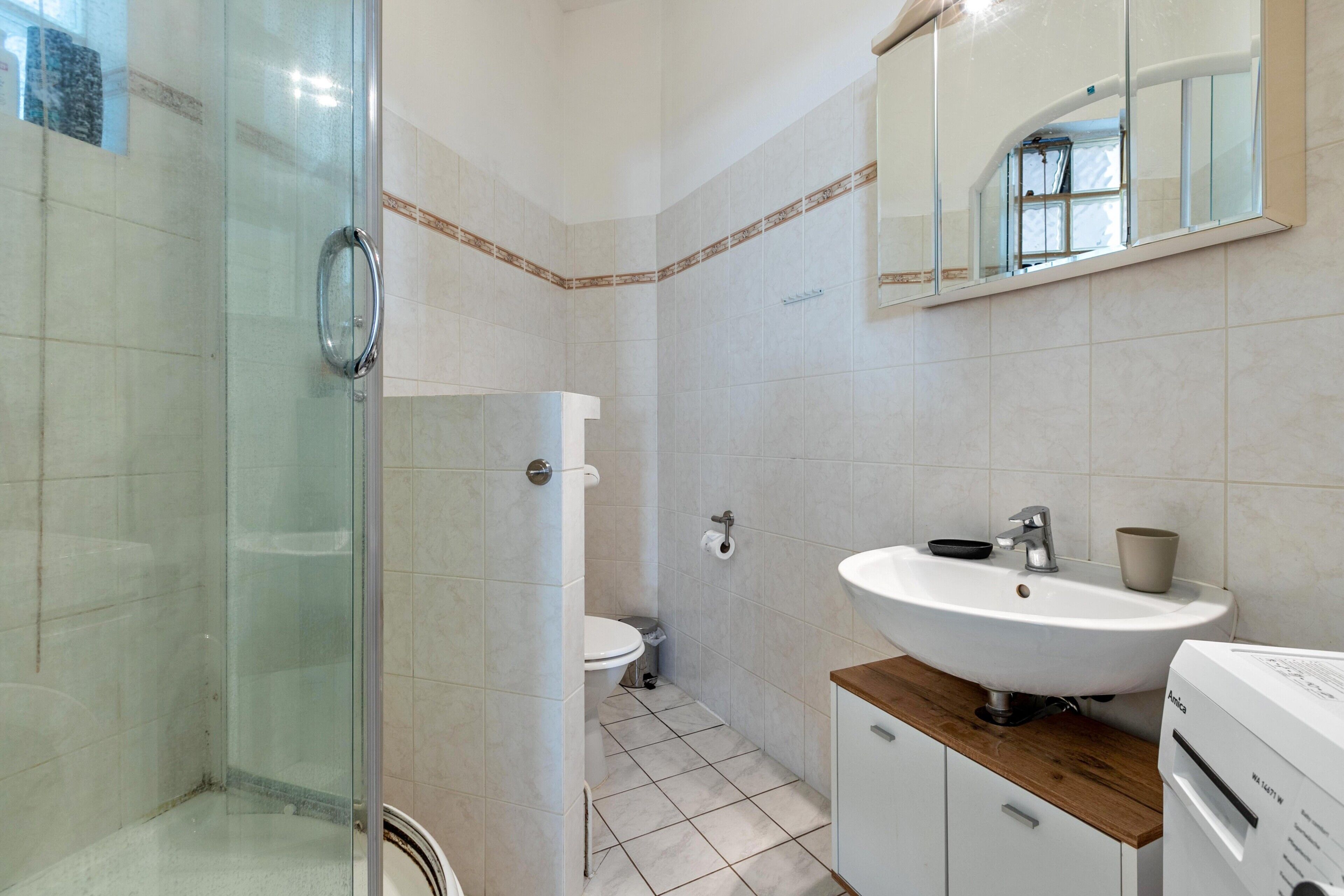 A bathroom with a glass shower enclosure, a toilet, a sink with a mirror above it, and a white cabinet.