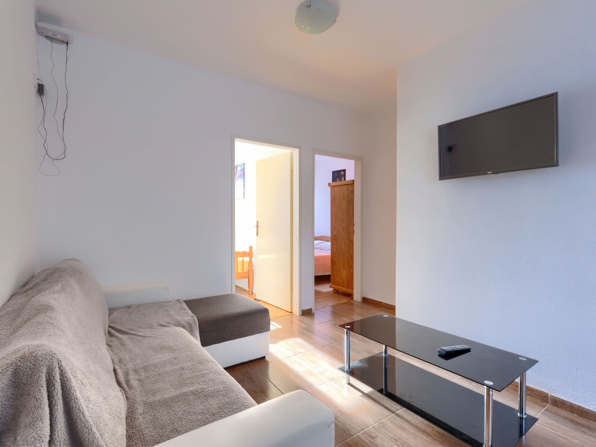 A modern living room with a sofa, a glass-top coffee table, and a flat-screen TV mounted on the wall.