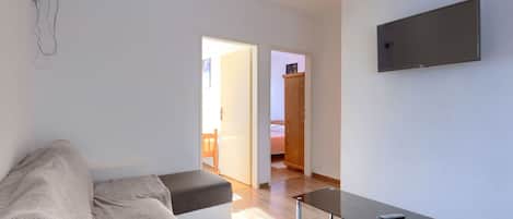 Una sala de estar moderna con un sofá, una mesa de centro de vidrio y un televisor de pantalla plana montado en la pared.