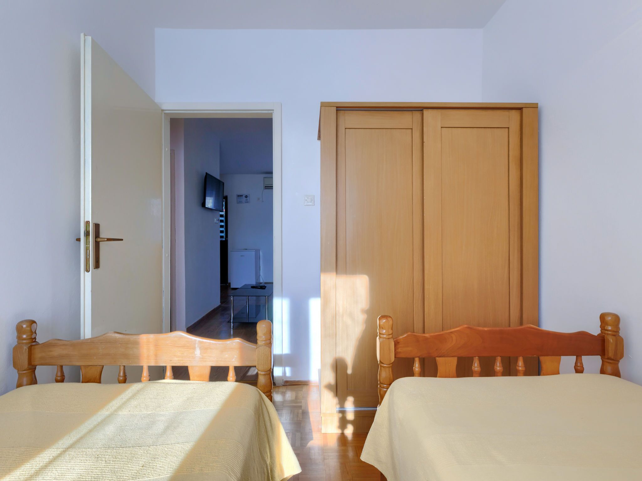 A bedroom with two wooden beds, a wardrobe, and a television in the adjacent room.