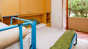 A room with a bed, wooden cabinets, a window with a view of trees, and a balcony.