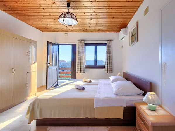 A bedroom with a wooden ceiling, a bed with white bedding, a bedside table with a lamp, and a view of the outside through a window. - Perkovic by Interhome (Medulin)