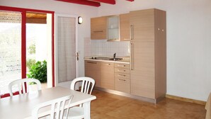 Eine kleine Küche mit Holzschränken, einem Spülbecken und einem Essbereich mit weißen Stühlen und einem Tisch.