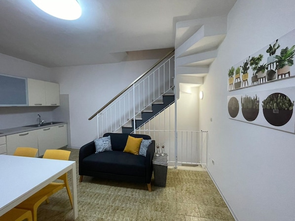 A compact living space with a kitchenette, a sofa, a dining table, and a staircase.