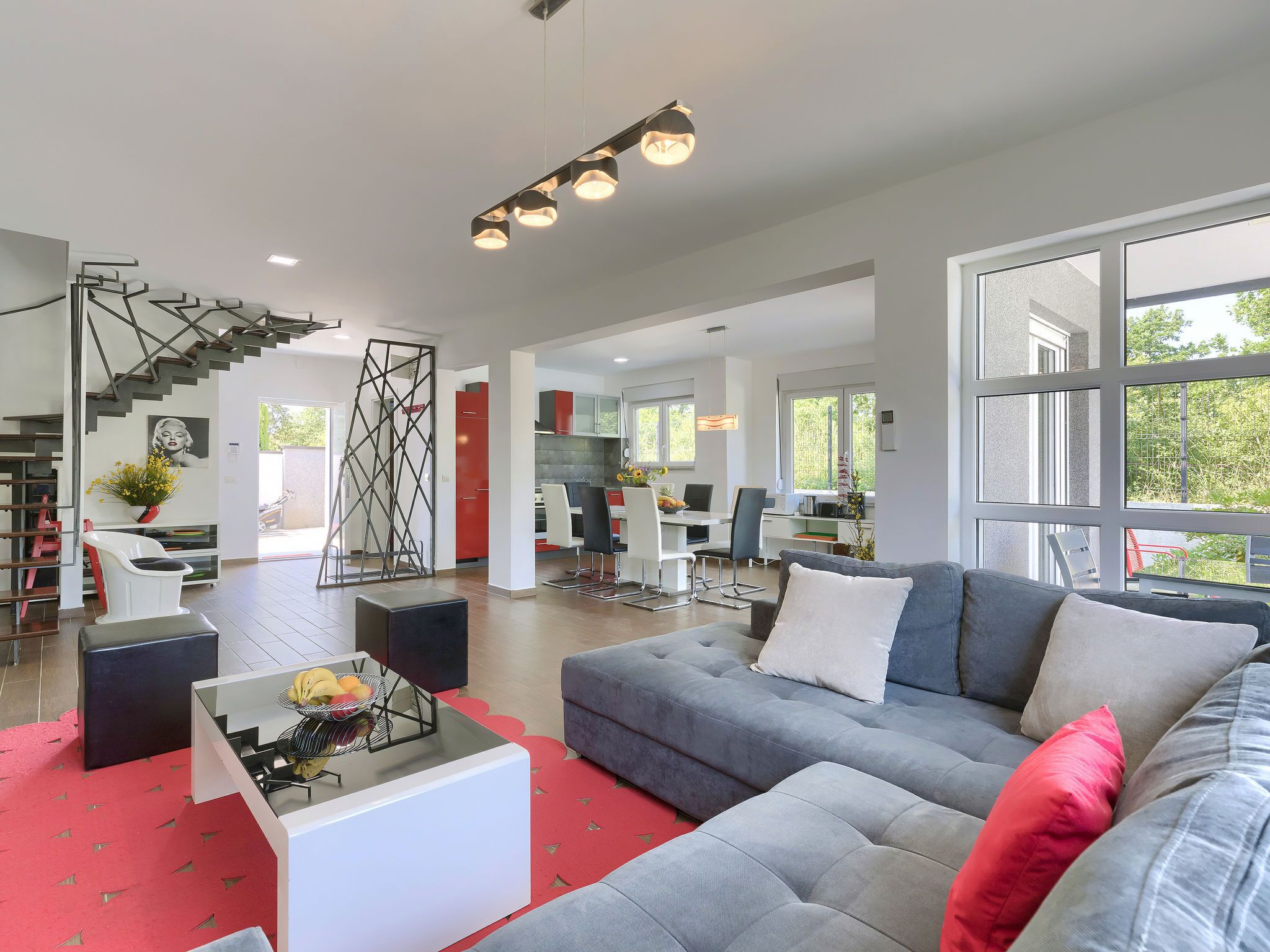 A spacious living area with a grey sofa, red accents, and a modern staircase.