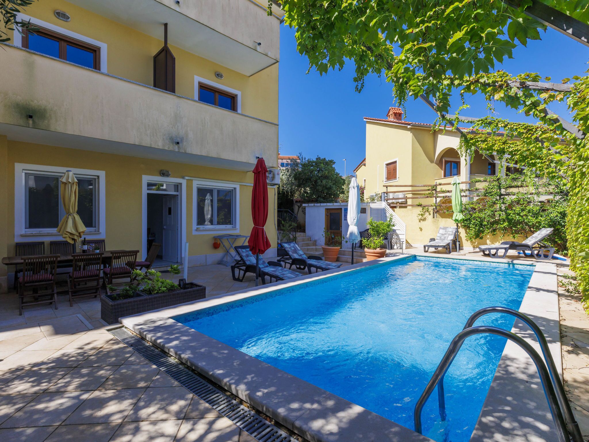 Une piscine entourée de bâtiments dotés de balcons et de fenêtres, avec des chaises longues et des parasols à proximité.