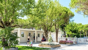 A building with a covered outdoor area, surrounded by trees and a white fence.