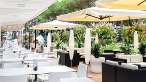 An outdoor cafe with white tables and chairs, yellow umbrellas, and potted plants.