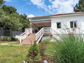 Uma casa de dois andares com varanda coberta, escada e quintal cercado.