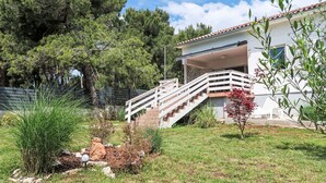 A house with a covered porch, a staircase leading to the entrance, and a fenced yard with trees and shrubs.