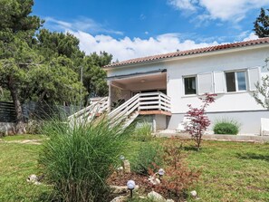 Uma casa de dois andares com varanda, escadaria e um jardim com diversas plantas.