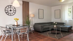 A modern living room with a dining table, chairs, a sofa, a small side table, and a clock on the wall.