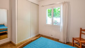 Un dormitorio con un armario grande, una ventana con cortinas, una alfombra azul y una silla de madera.