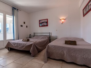 Une chambre avec deux lits, une fenêtre avec des rideaux, un luminaire fixé au mur et un tableau encadré.