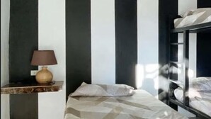 Una stanza con un letto a castello, un comodino con una lampada e una coperta con motivo geometrico.