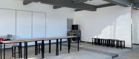Ein Außenbereich mit einer langen Tafel und mehreren Stühlen, einem Fernseher und einem Lautsprecher.