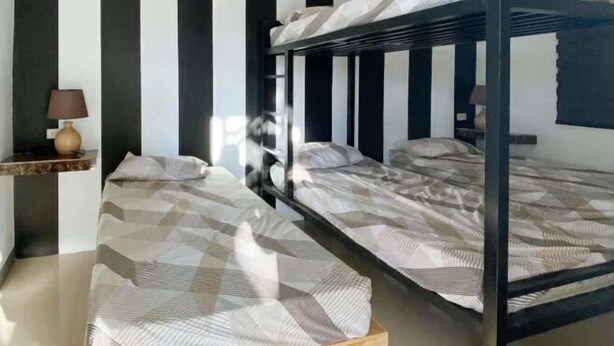 Une chambre avec deux lits superposés, une petite table de chevet avec une lampe et une fenêtre avec des stores verticaux.