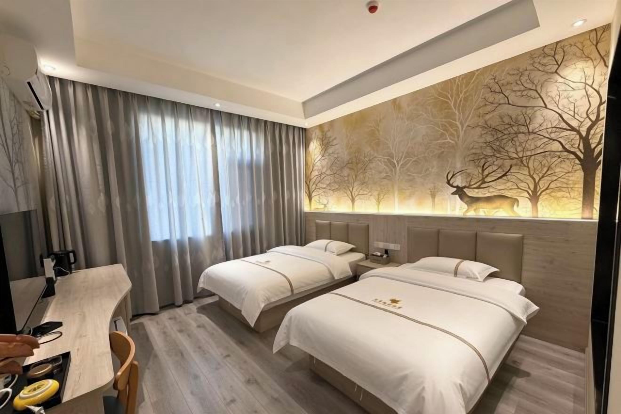 A hotel room with two beds, a desk, and a large window with curtains.
