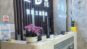 A hotel reception desk with a potted purple orchid, a signboard, and a wall-mounted clock. - Orchid Smart Theme Hotel (Qiaojia)
