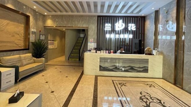 Zona de recepción de un hotel con un mostrador de mármol, un sofá y una escalera al fondo.