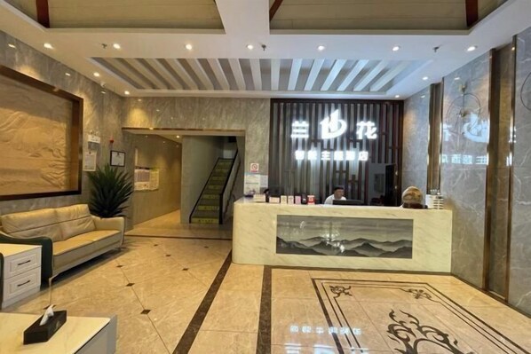 A hotel reception area with a marble reception desk, a sofa, and a staircase in the background. - Orchid Smart Theme Hotel (Qiaojia)