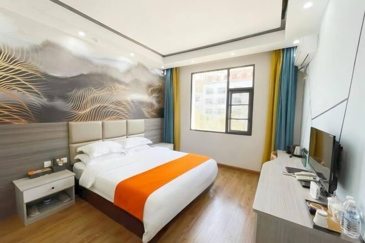 Habitación de hotel con cama, mesita de noche, escritorio y un ventanal grande.
