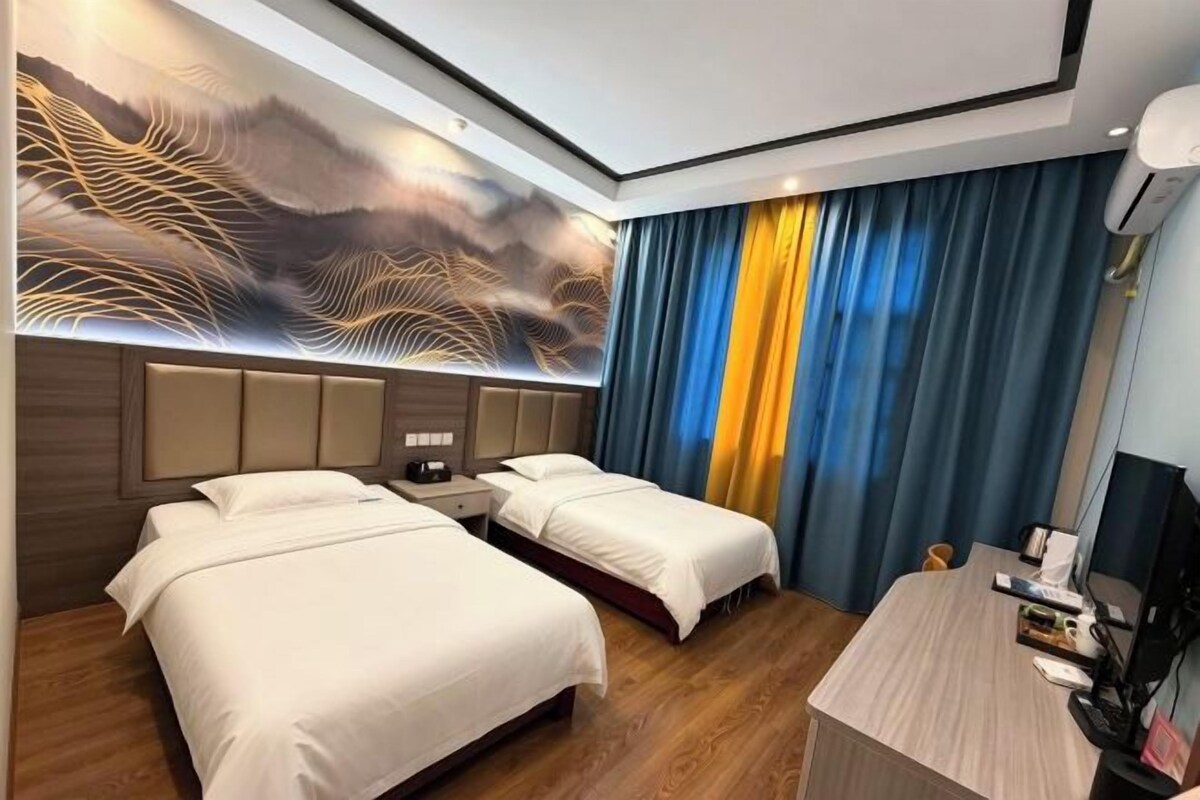 A hotel room with two beds, a desk, and a wall-mounted artwork.