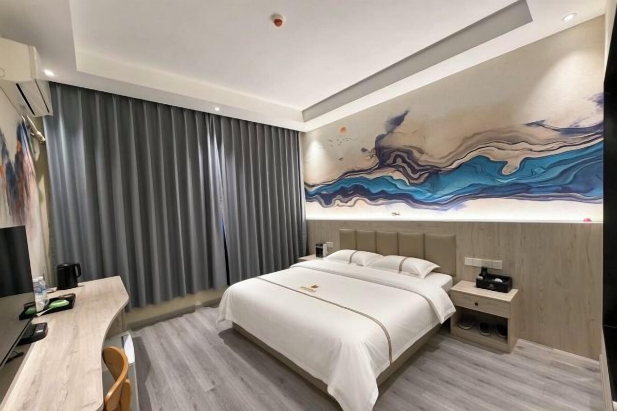 A modern hotel room with a large bed, a desk, and a wall-mounted artwork.