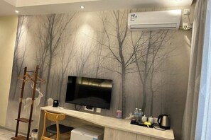 A room with a flat-screen TV, a desk with a chair, a coat rack, and a wall-mounted air conditioner. - Orchid Smart Theme Hotel (Qiaojia)