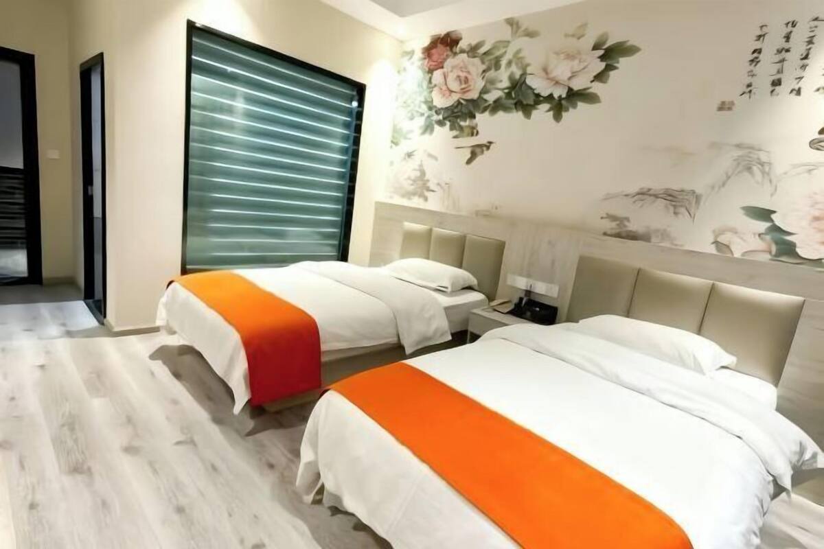 Habitación de hotel con dos camas, un ventanal con persianas, una pared con arte floral y de caligrafía, y piso de madera.