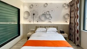 A modern hotel room with a large bed, a green sliding door, a wall with abstract designs, and a patterned curtain. - Orchid Smart Theme Hotel (Qiaojia)