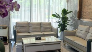A modern living room with a beige leather sofa, a glass coffee table, and a large green plant. - Orchid Smart Theme Hotel (Qiaojia)