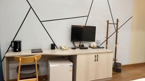 A modern office space with a desk, chair, and a small refrigerator. - Orchid Smart Theme Hotel (Qiaojia)