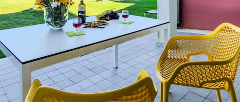 A table set with a bottle, wine glasses, grapes, and a plate of breadsticks on a balcony with yellow chairs and a view of a residential area.