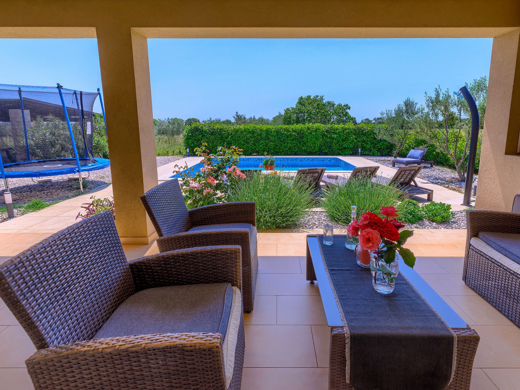 Ein überdachter Patio-Bereich mit Korbmöbeln, einem Pool und Blick auf die umliegende Bepflanzung.