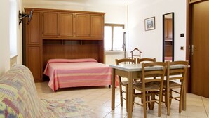 A bedroom with a bed, a desk, chairs, a wardrobe, and a window.