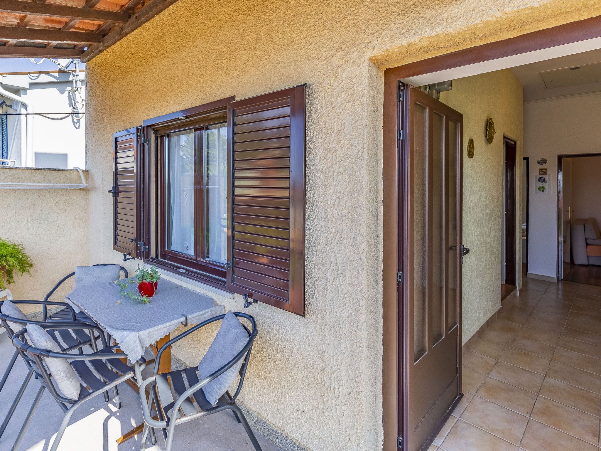 An outdoor patio with a table and chairs, a potted plant, and a door leading to an interior space.