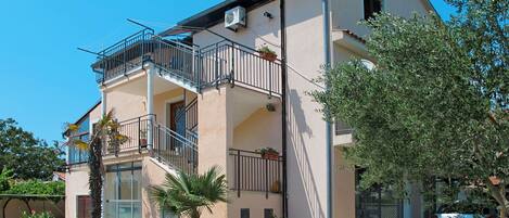 A two-story building with balconies, a staircase, and a car parked in front.