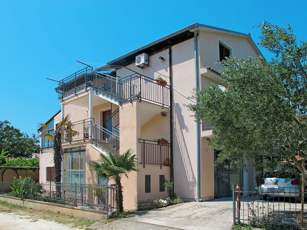 A two-story building with balconies, a staircase, and a car parked in front.