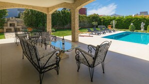 A covered outdoor area with a pool, lounge chairs, and a dining table with chairs.