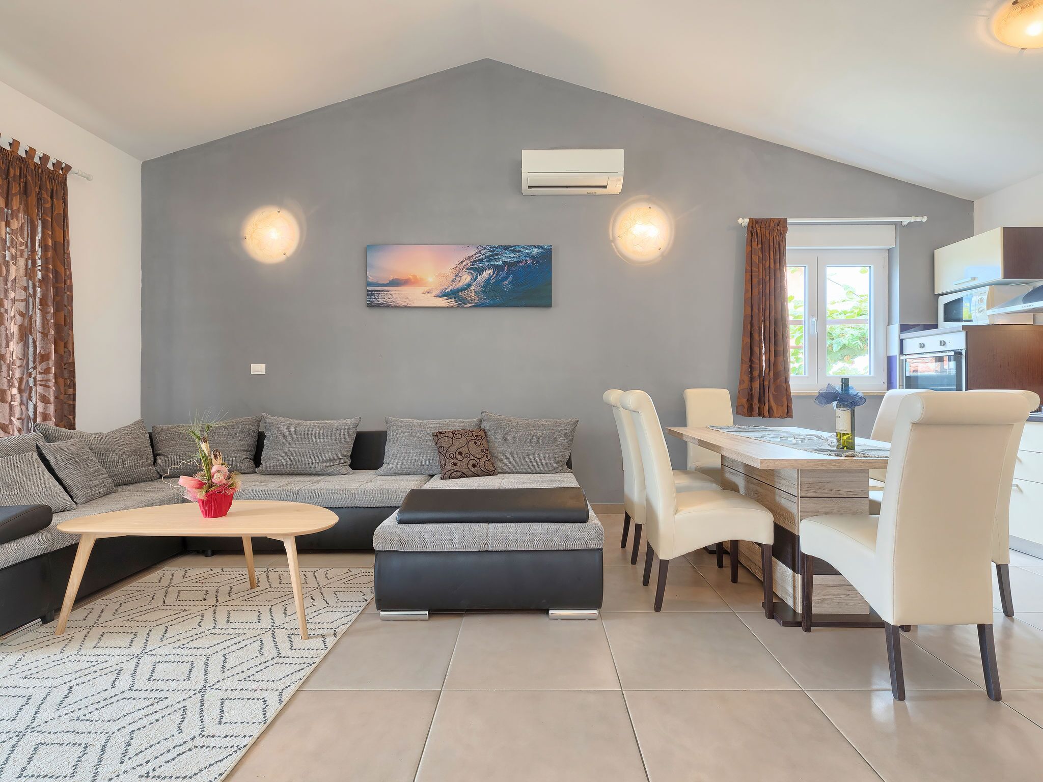 A modern living room with a grey sofa, a dining table with chairs, a coffee table, and a painting on the wall.